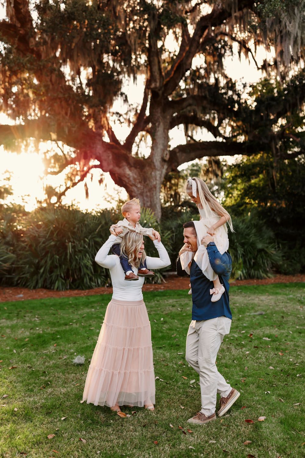 A couple dances playfully together on a grassy lawn at sunset with Spanish moss hanging from trees in the background.