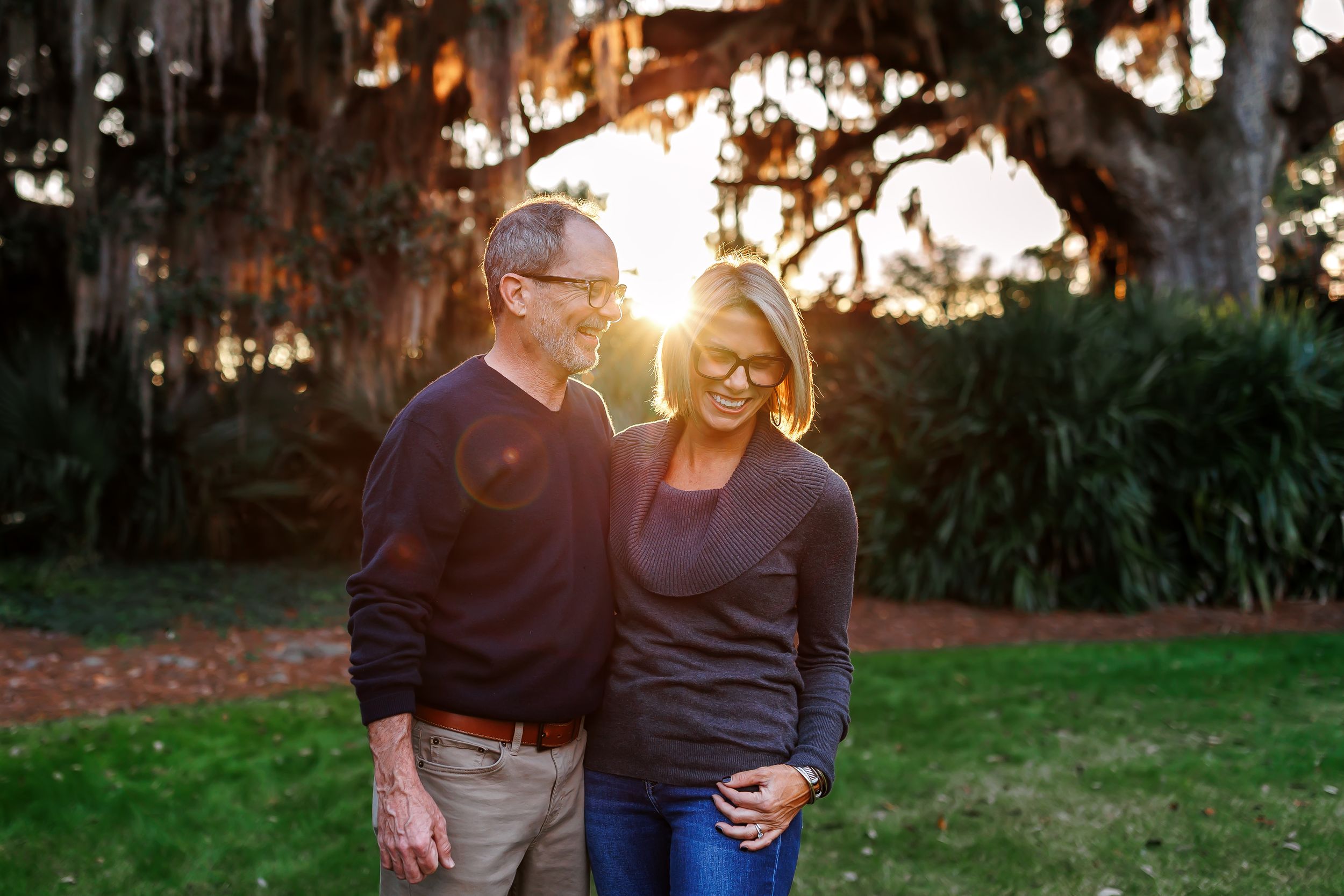 A couple sits together outdoors during golden hour as sunlight filters through trees in the background.