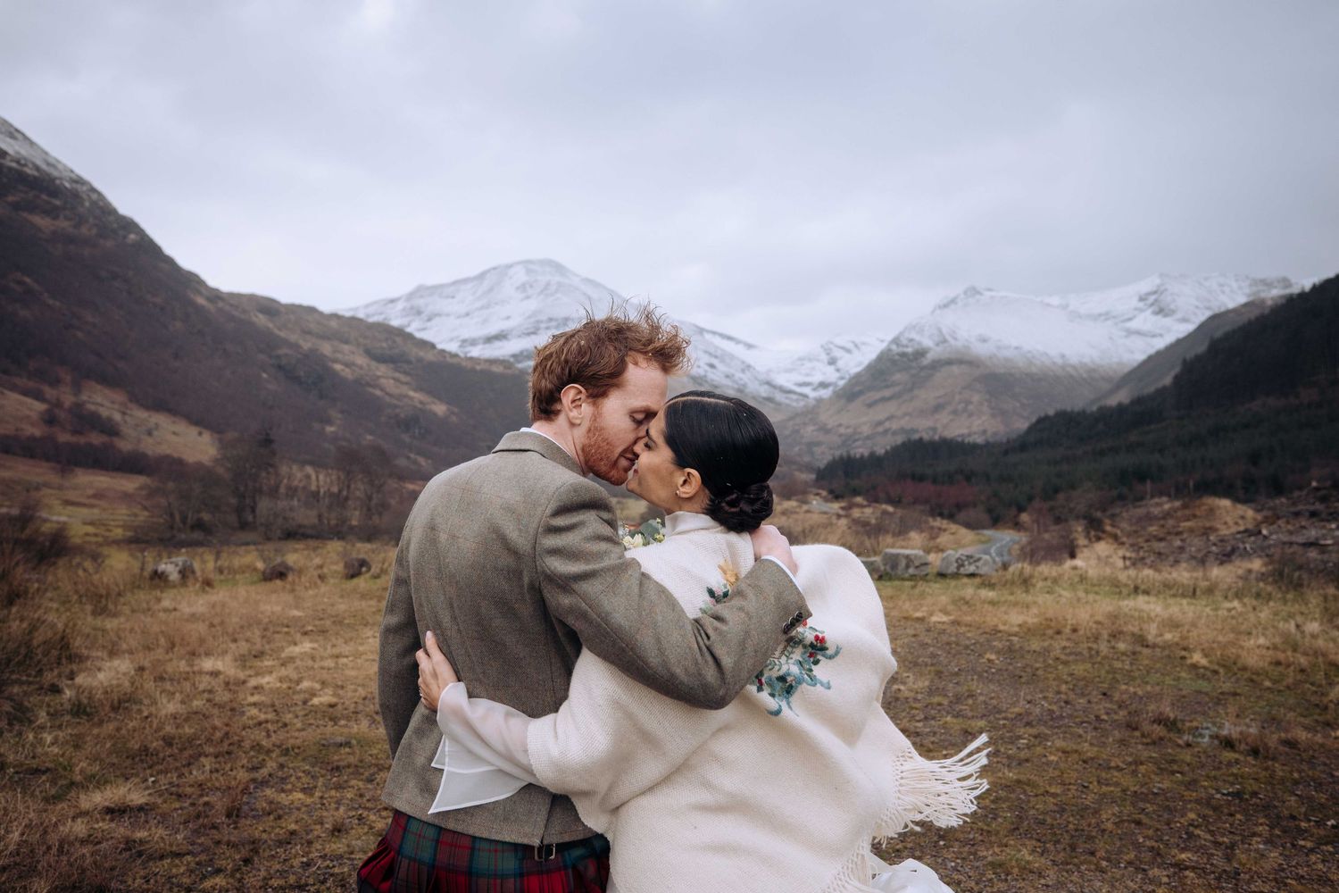A couple walks hand in hand down a remote road in the Scottish highlands.