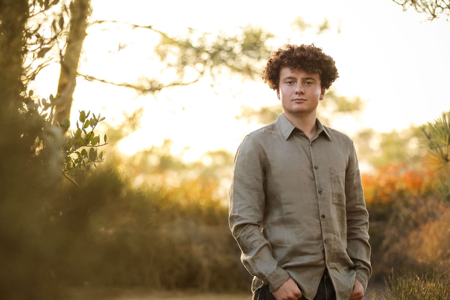 A high school senior stands beside a white building during golden hour with cactus plants in the foreground.