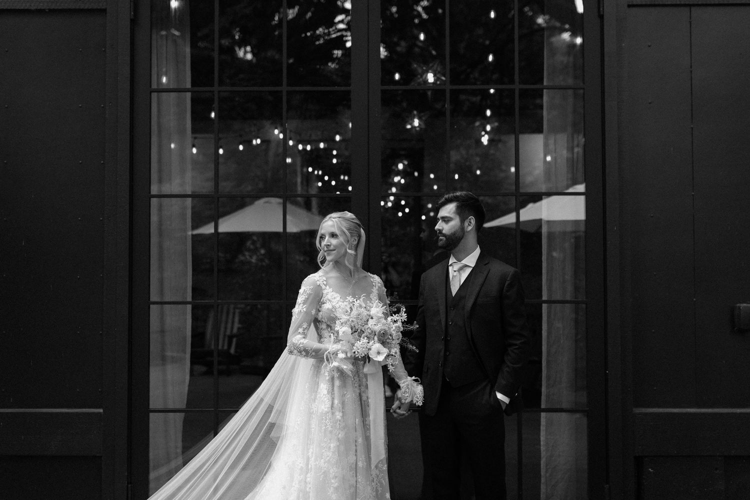 Black and white wedding portrait with string lights creating romantic ambiance.