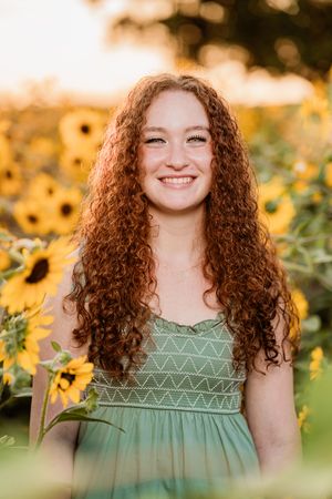 Portrait in a sunflower field at golden hour featuring long curly red hair and a sage green dress with geometric patterns.
