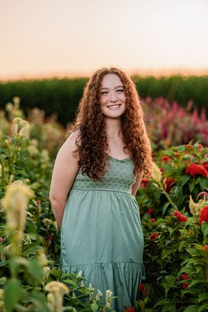 A person in a mint green summer dress stands among blooming red flowers in a garden at sunset.
