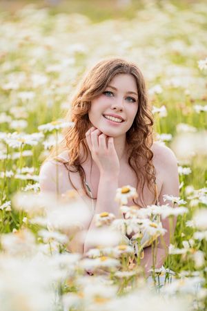 Person sits among blooming daisies in a meadow during warm golden sunset light.