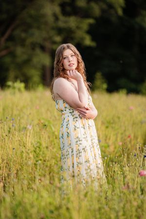 A person in a yellow floral sundress stands thoughtfully in a summer meadow filled with wildflowers.