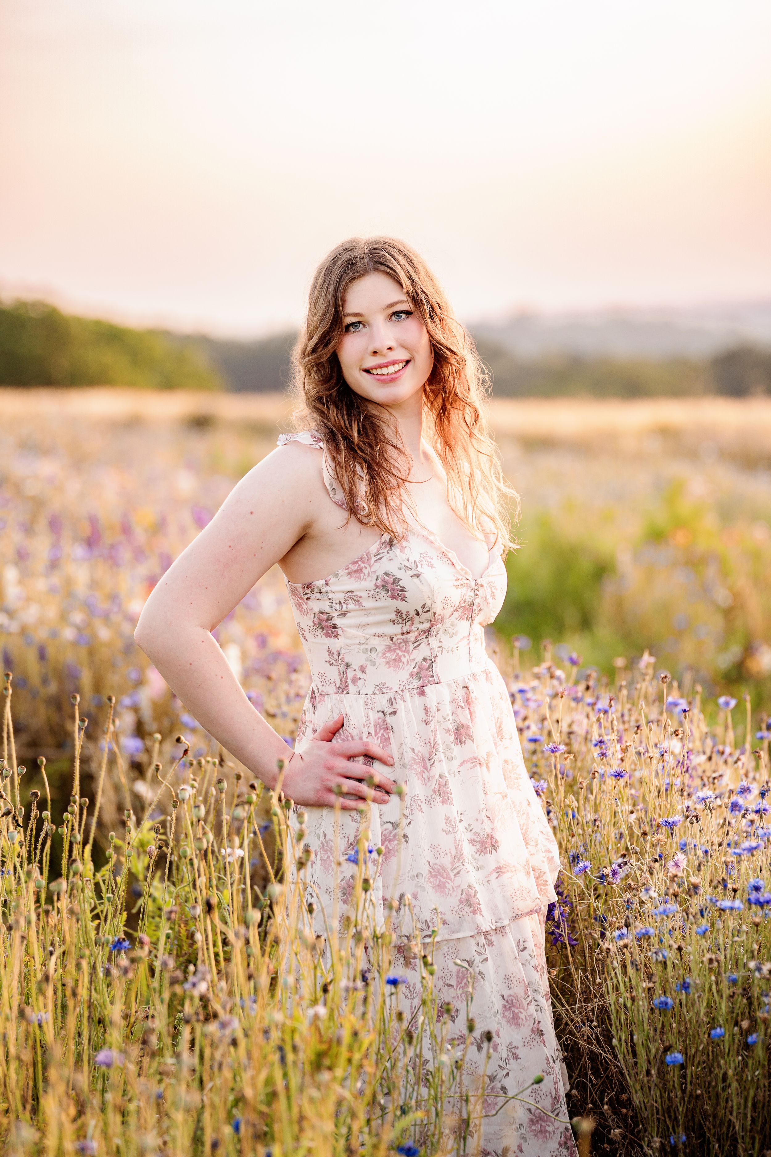 A person in a floral dress poses in a lavender field at sunset during golden hour.