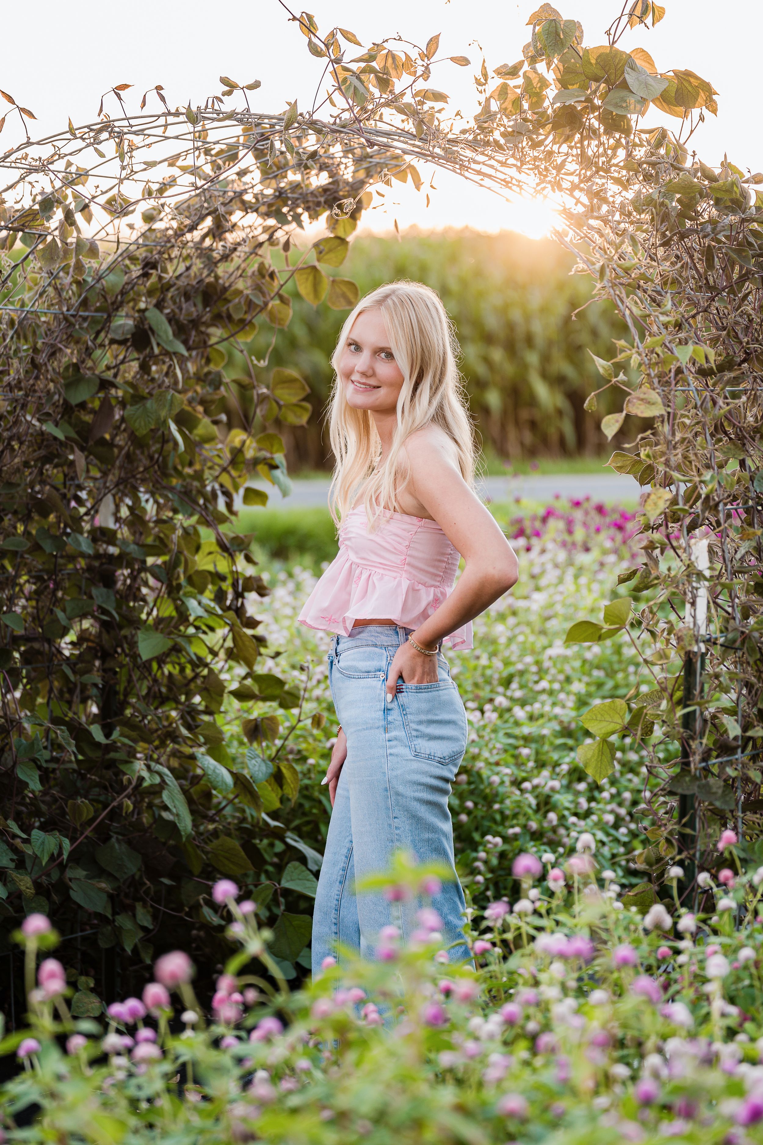 Portrait in blooming garden arch during golden hour with soft sunlight filtering through flowers.