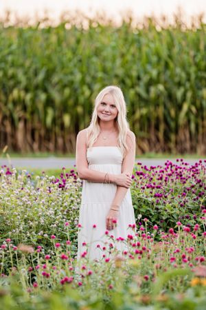 Portrait among vibrant purple flowers with cornfield backdrop during sunset.