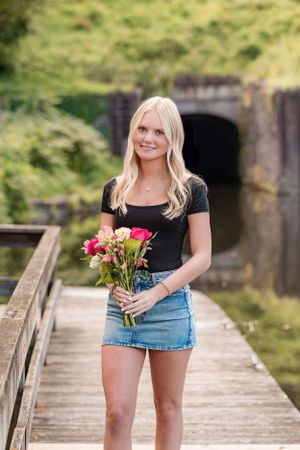 Portrait on wooden bridge holding colorful bouquet with rustic tunnel backdrop.