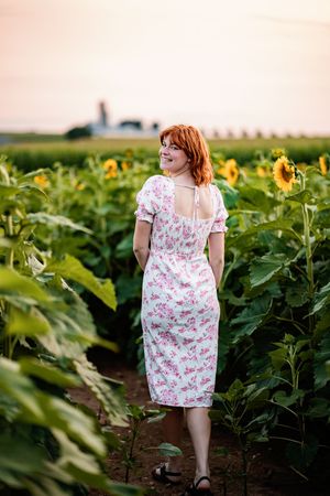 A figure in a floral dress explores a vibrant sunflower field on a sunny afternoon.