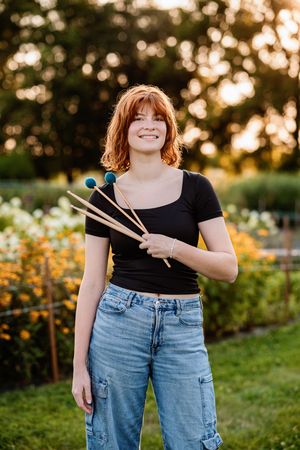 Person wearing black top and blue jeans stands in a garden with golden sunlight and yellow flowers at sunset.