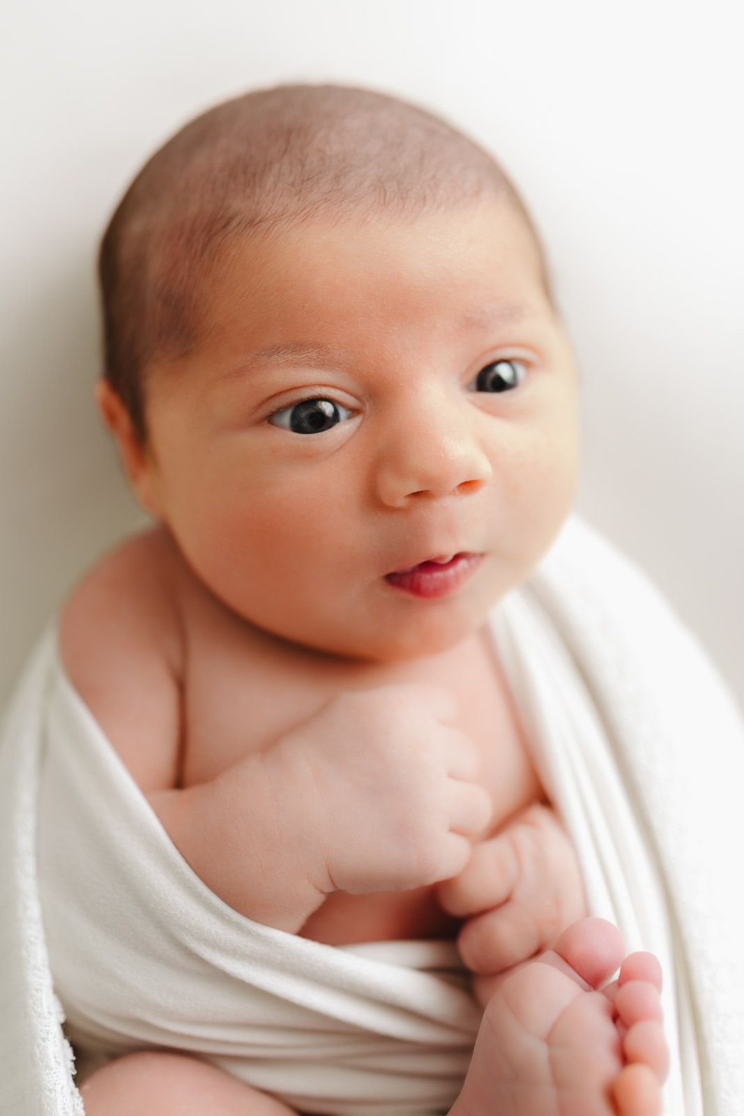 A series of close-up portraits showing a newborn baby wrapped in white fabric expressing different gentle expressions.