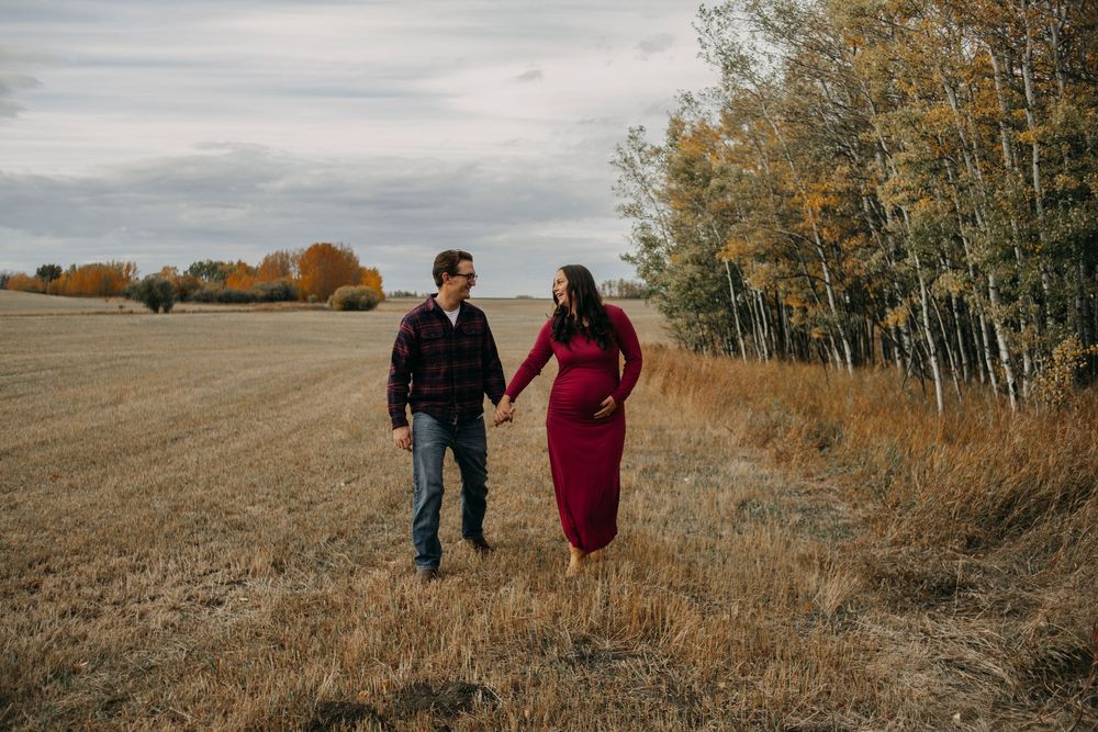 Couple walking together through autumn fields and trees in warm golden light during sunset.