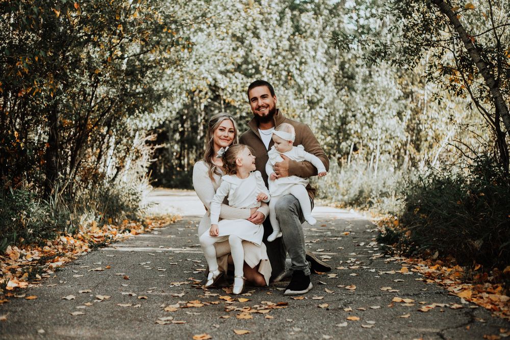 Family portrait taken on a tree-lined autumn path with fallen leaves.