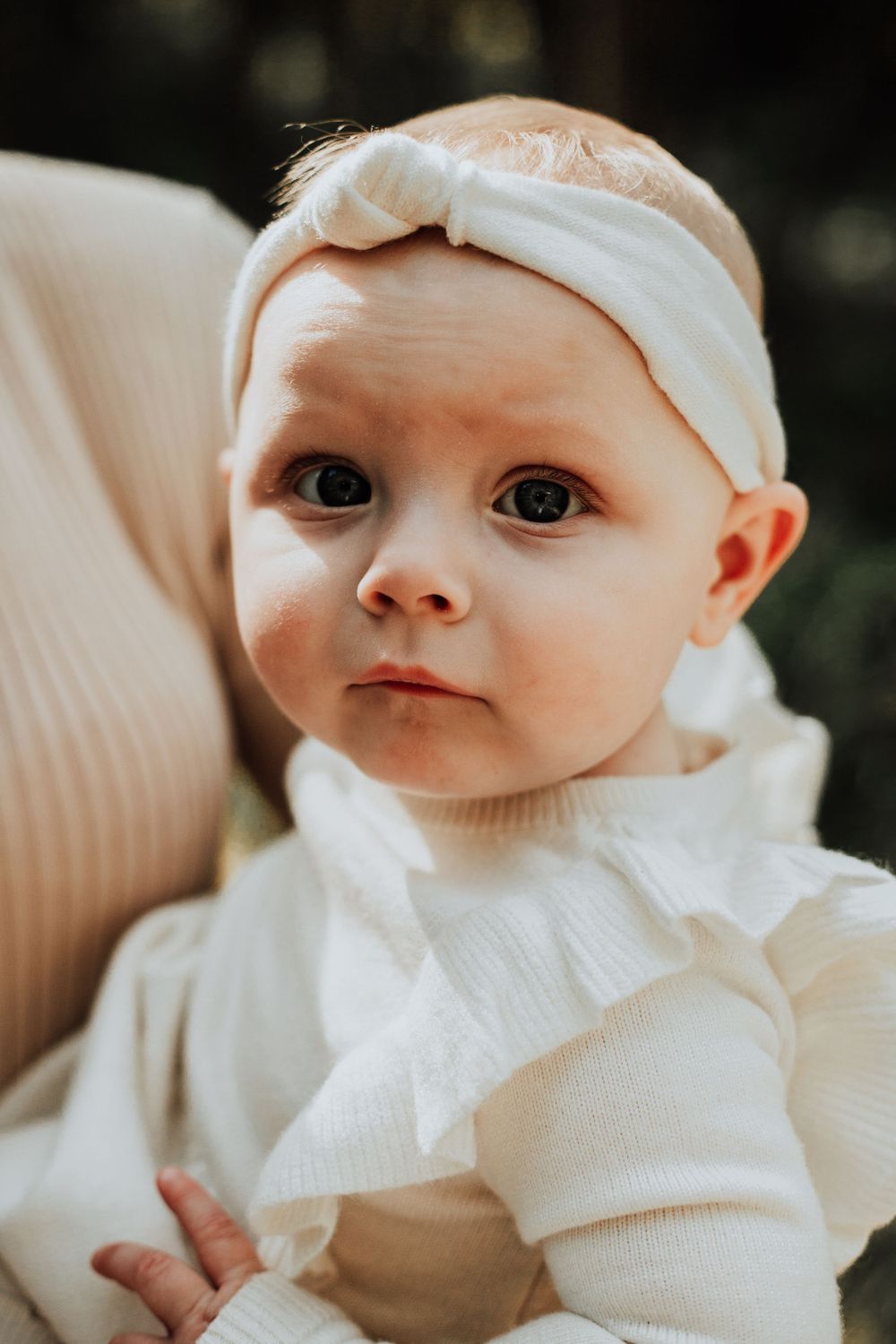 Close-up portrait of baby wearing white knit outfit and headband.