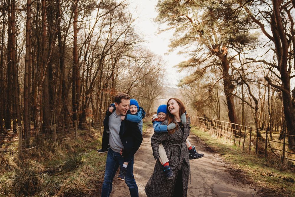 Happy family with two young children walking together on a woodland path surrounded by autumn trees.