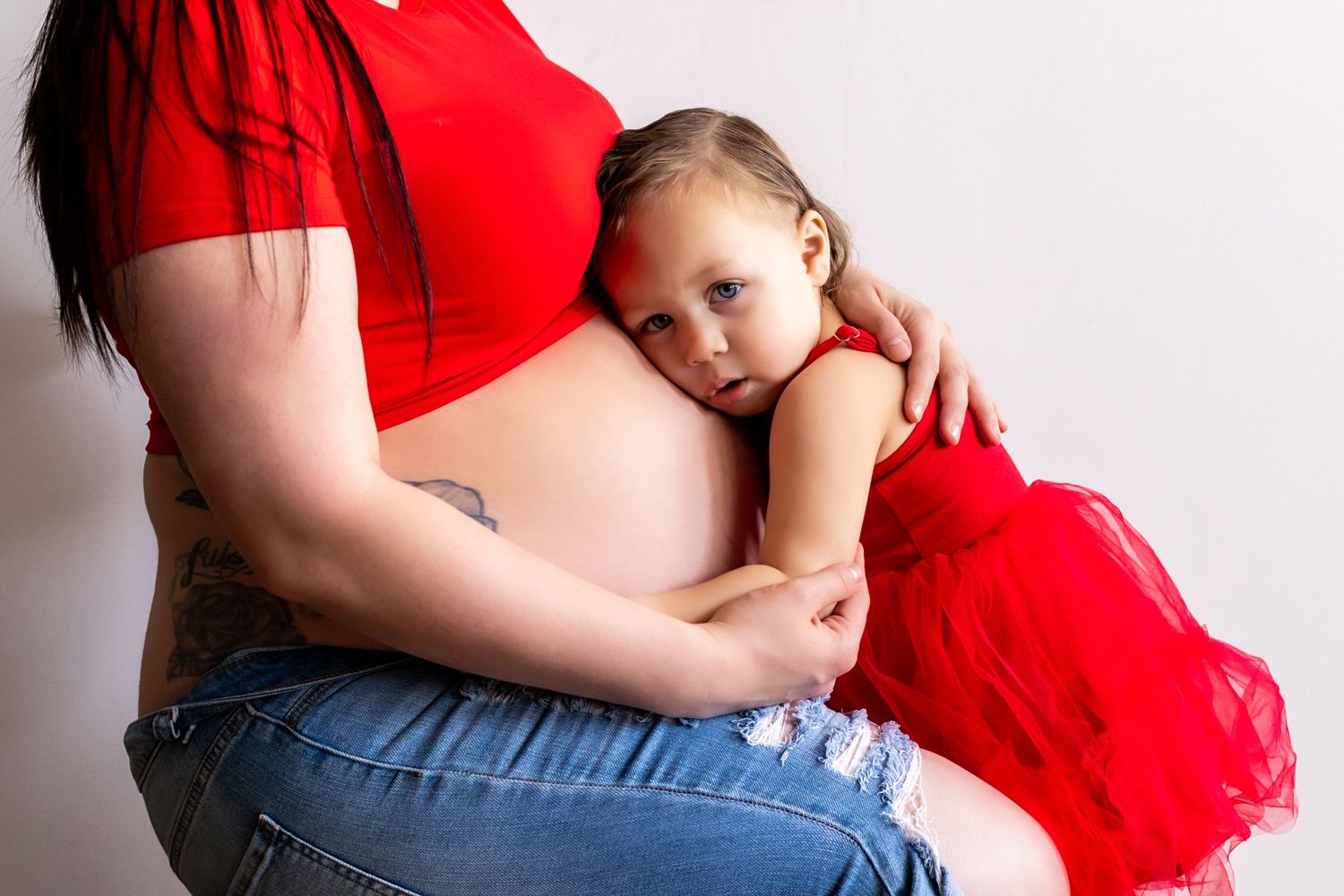 Maternity photo showing small child hugging mother's pregnant belly while both wear red.