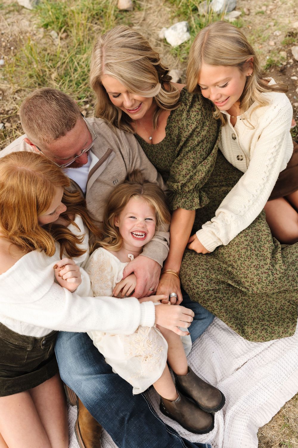 A joyful family of five cuddles together outdoors, laughing and smiling in a warm, candid portrait.