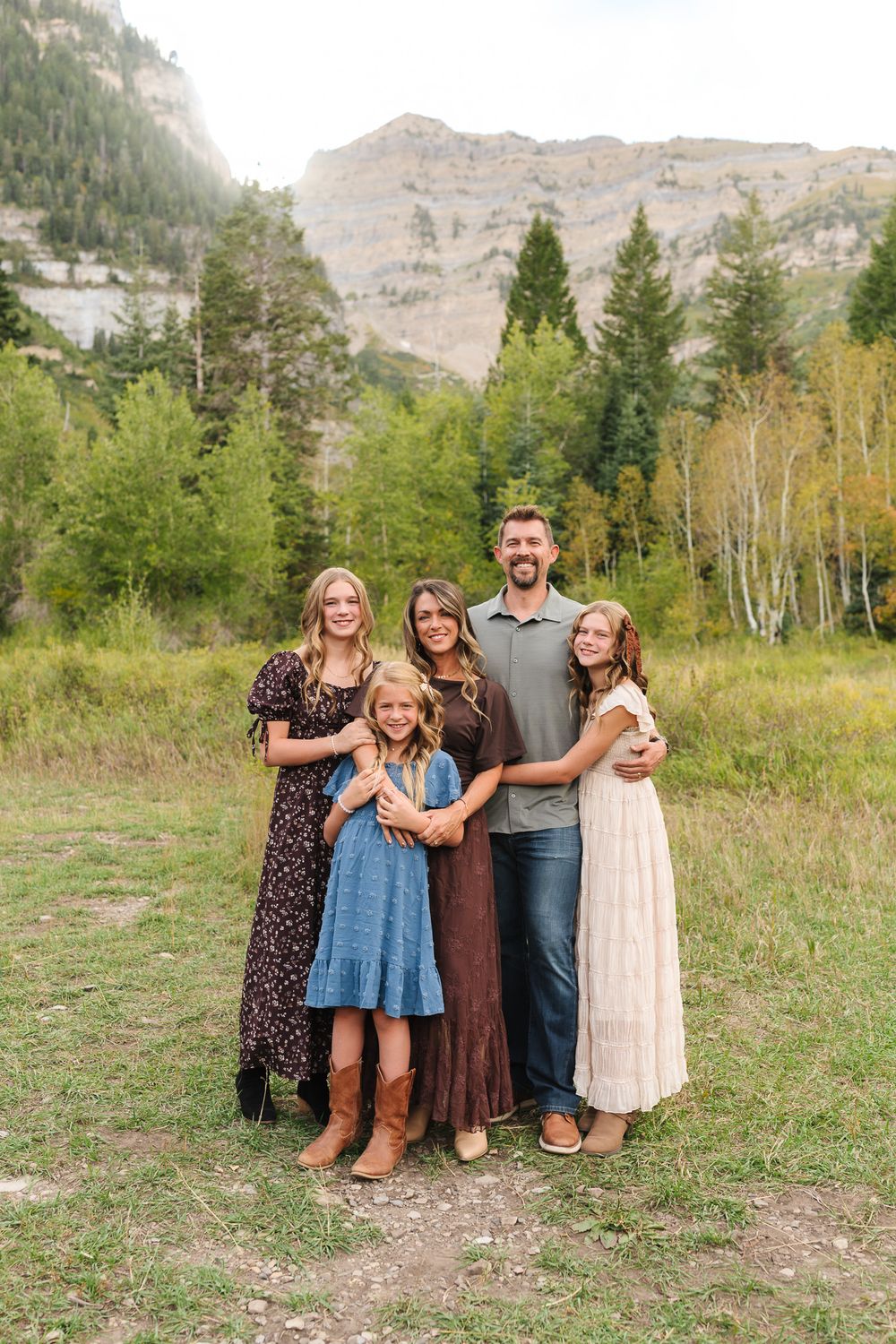 Family of five posing together in a mountain meadow surrounded by pine and aspen trees during fall season.