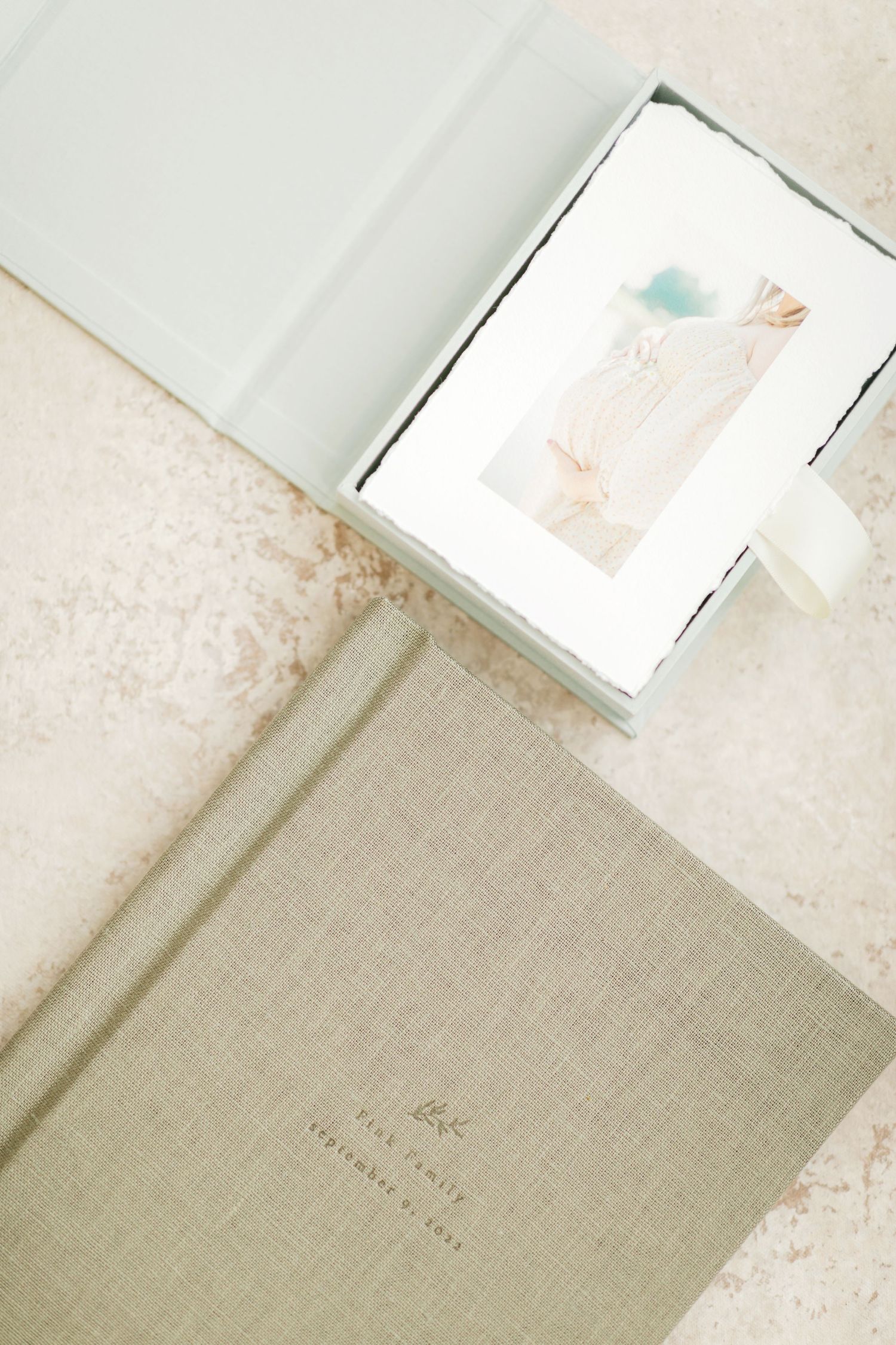 Elegant sage green linen wedding album beside an open keepsake box with watercolor print on marble surface. Printed heirloom products