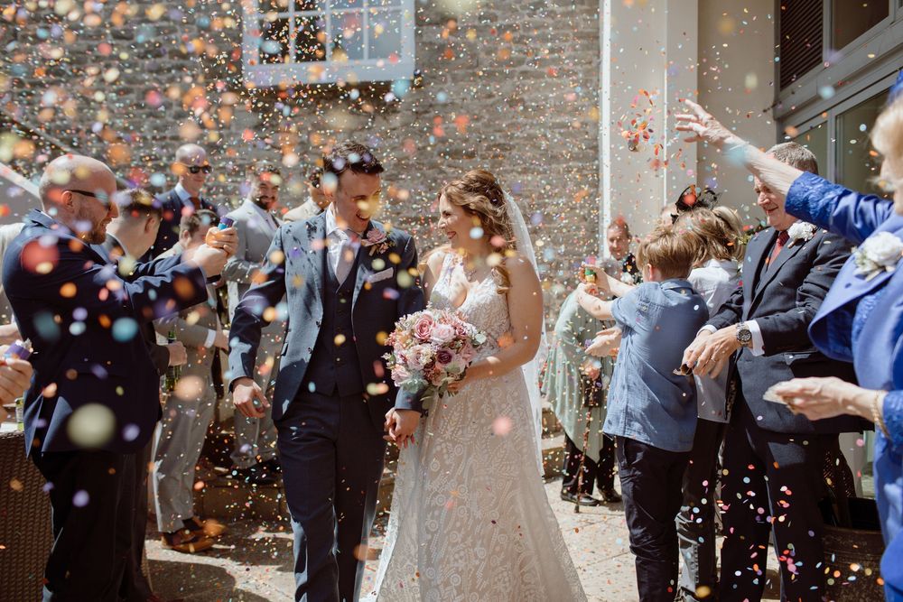 Married couple walking through a swarm of colourful confetti at The Bear Hotel Cowbridge in South Wales.