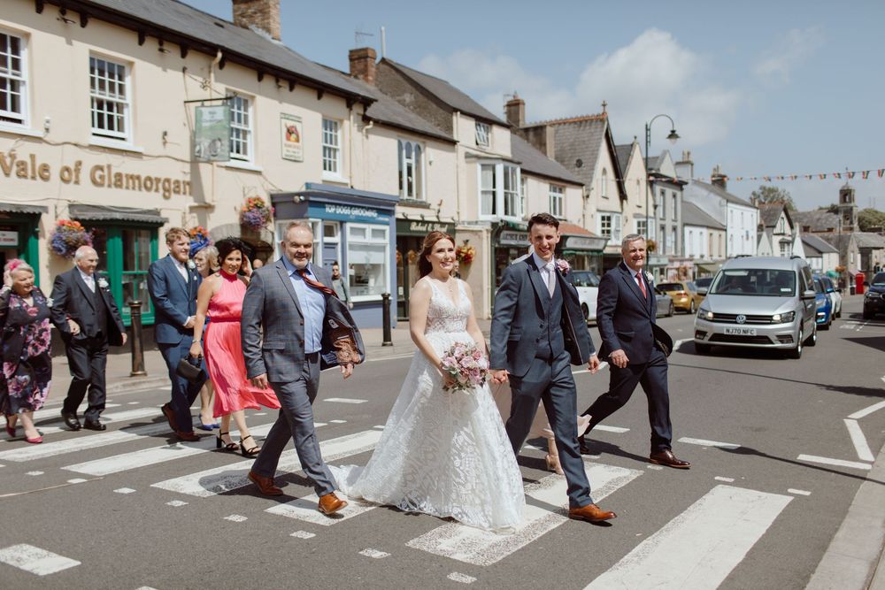 A married couple and family walking over a zebra crossing during a wedding at The Bear Hotel in Cowbridge.
