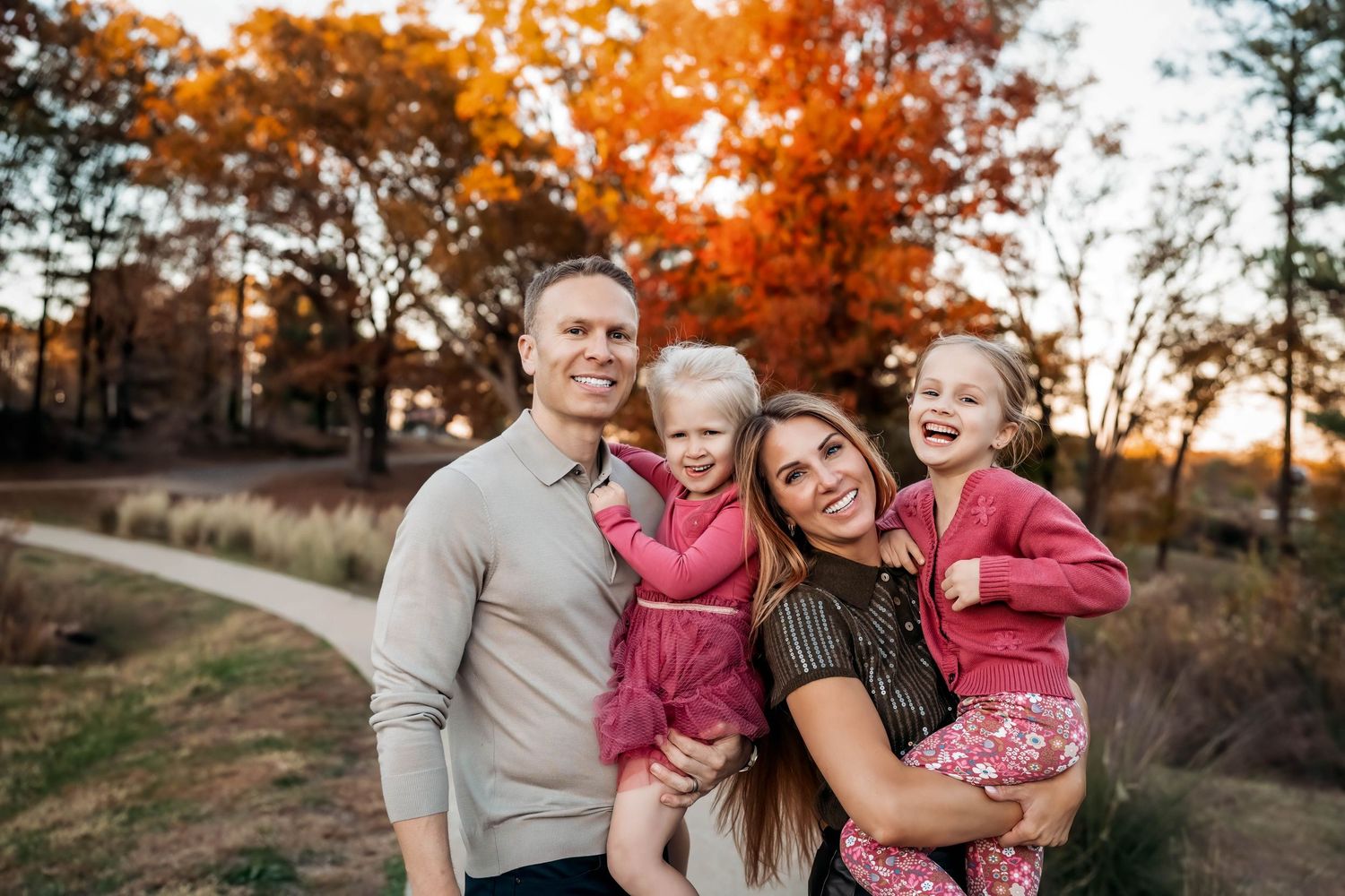 Family in coordinating pink and grey outfits share joyful moments during an autumn sunset photoshoot.