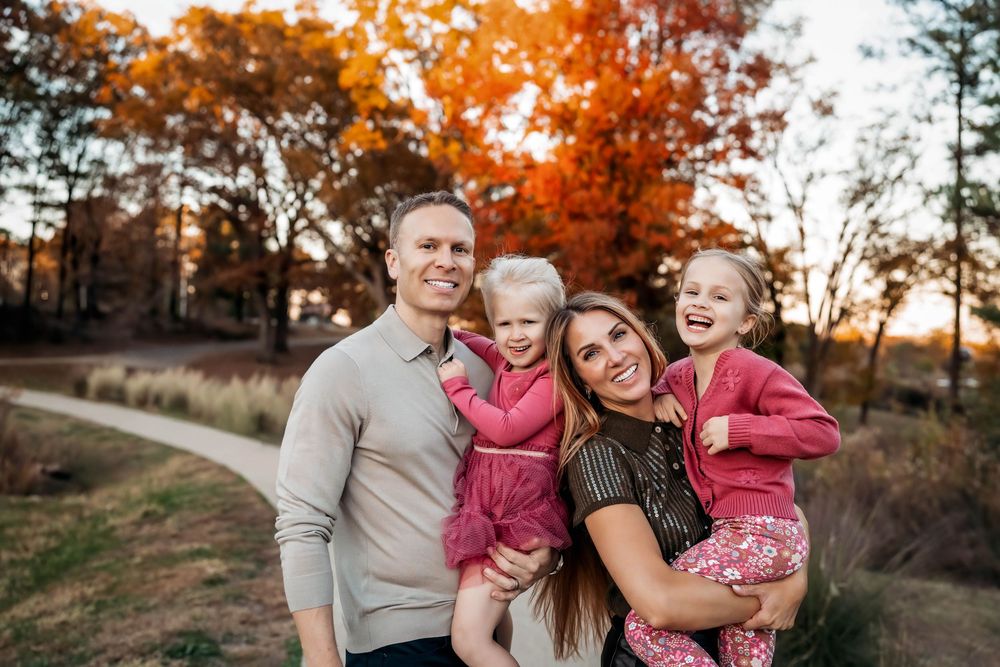Family in coordinating pink and grey outfits share joyful moments during an autumn sunset photoshoot.