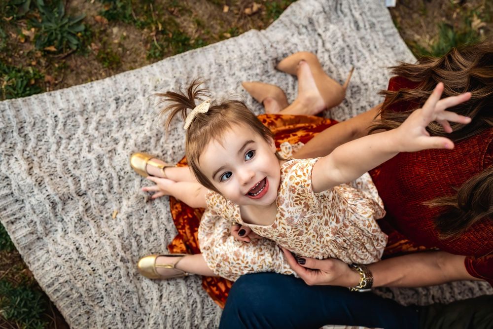 A young child lays on a white blanket with scattered autumn leaves in an outdoor photo session.