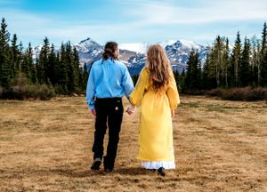 Couple in blue and yellow outfits viewing mountain landscape from meadow.