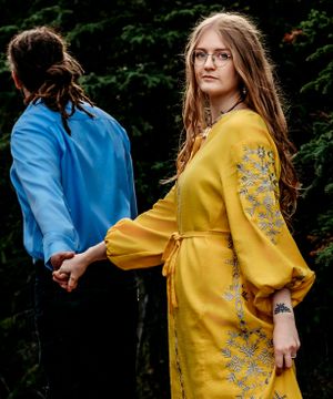 A close up view of a yellow embroidered dress with puff sleeves and floral details in a forest setting.