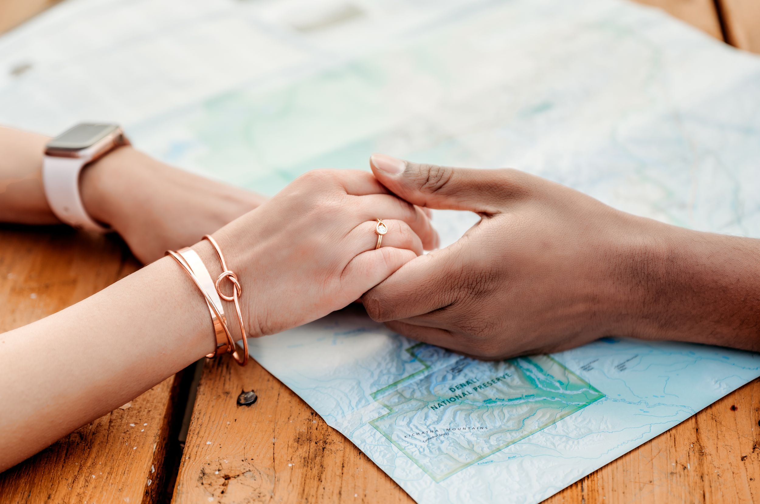 Hands with engagement ring rest on a map on wooden table.