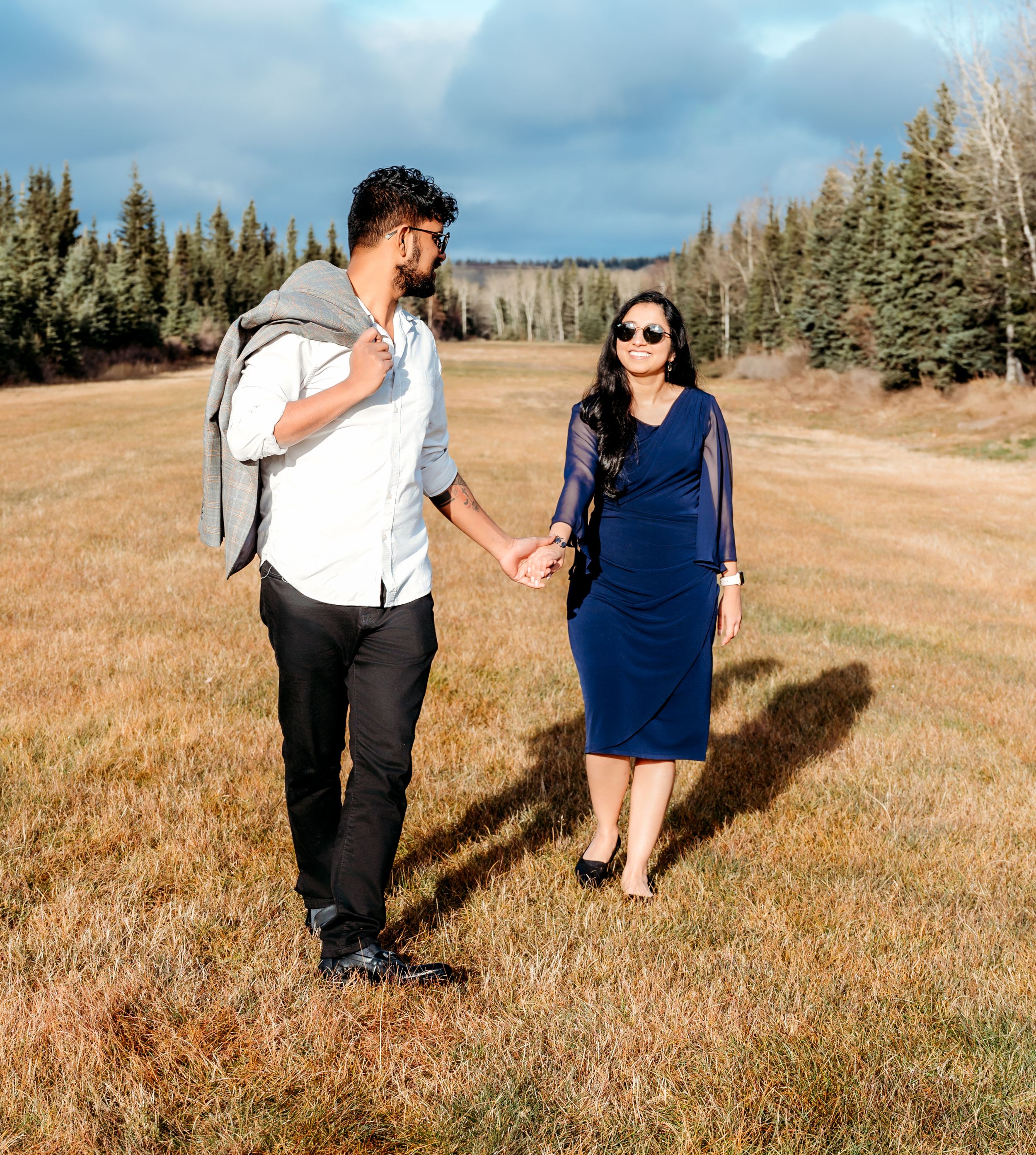 A couple walking through a mountain meadow surrounded by pine trees.