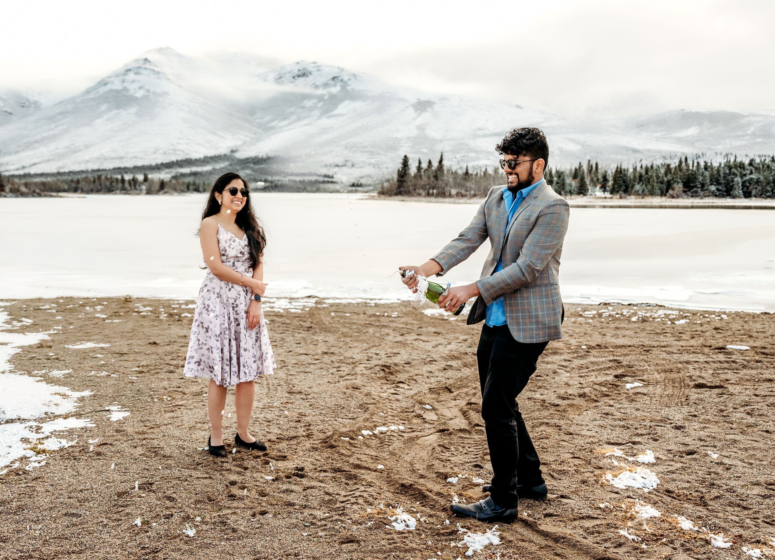 A romantic moment captured against snowy mountains and evergreen trees.