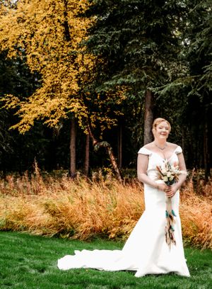 Outdoor autumn wedding photo with golden foliage and tall trees in background.