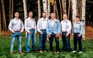 Groomsmen in light blue and white attire posed casually against forest backdrop.