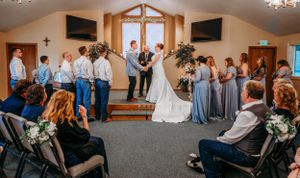 Wide view of wedding ceremony in church with wedding party in blue and gray attire.