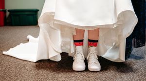Wedding dress hem lifted to reveal red and white sneakers underneath.