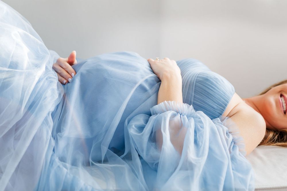 A person in a flowing light blue tulle dress lies gracefully on a light colored surface.