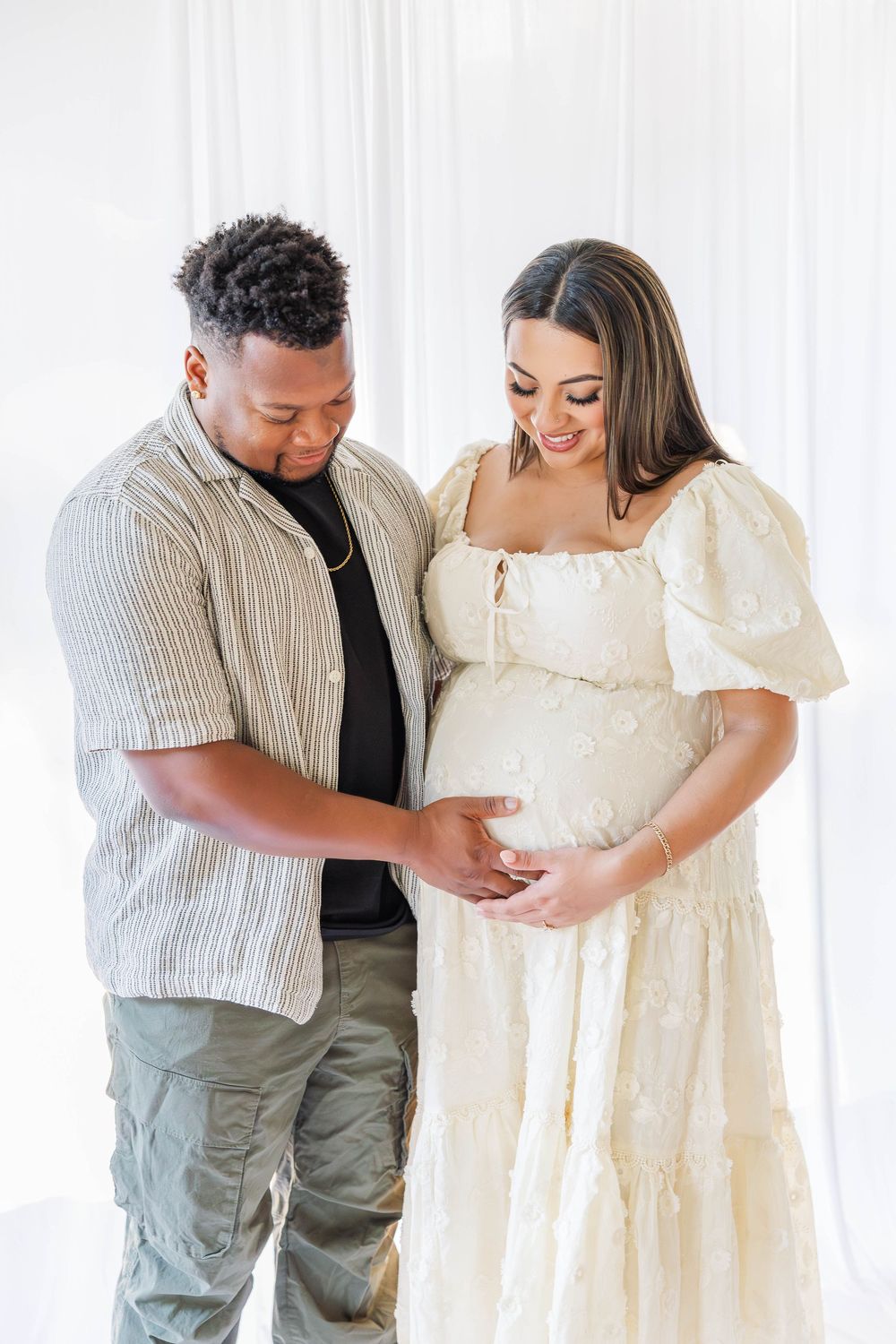 A couple shares an intimate moment in a bright studio setting wearing casual and white formal attire.
