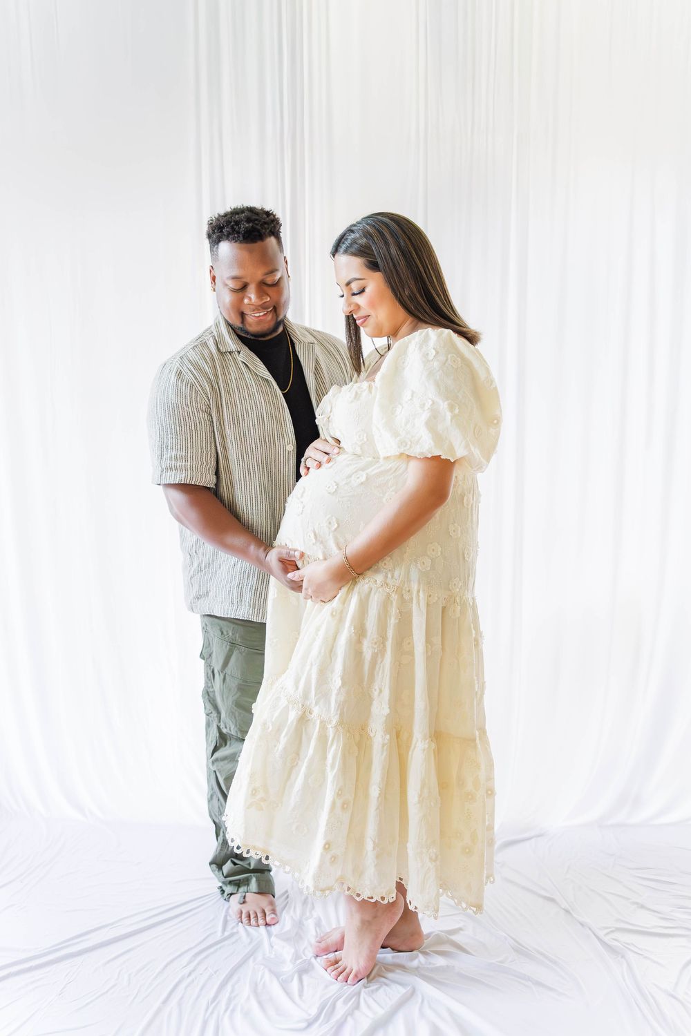 A couple shares an intimate moment in a bright white studio setting while wearing casual and flowy clothing.
