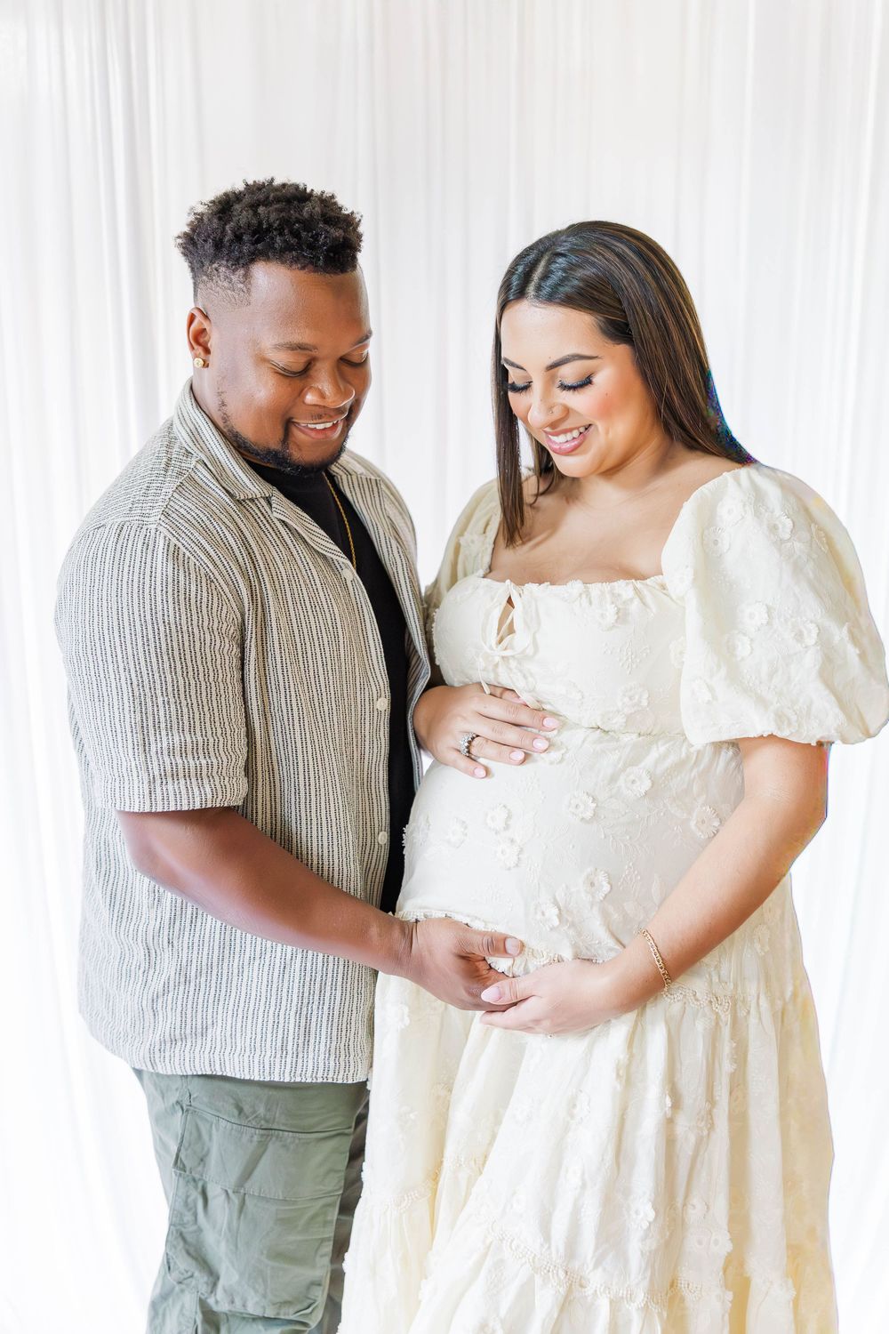 A couple shares an intimate moment during a maternity photoshoot against a white backdrop.