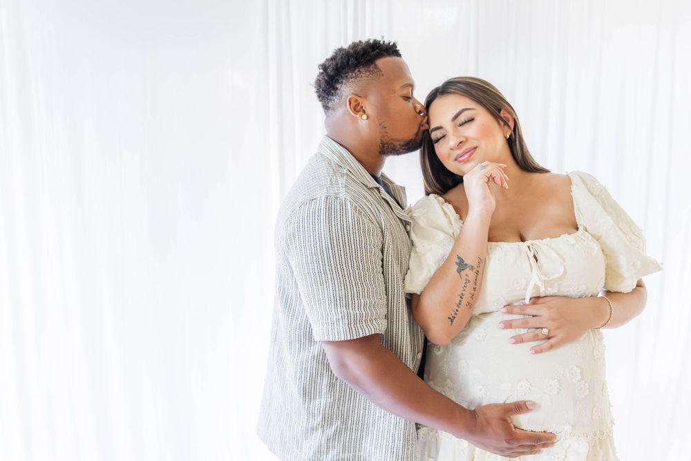 A tender moment between a couple in white and stripes as they embrace near a bright window.