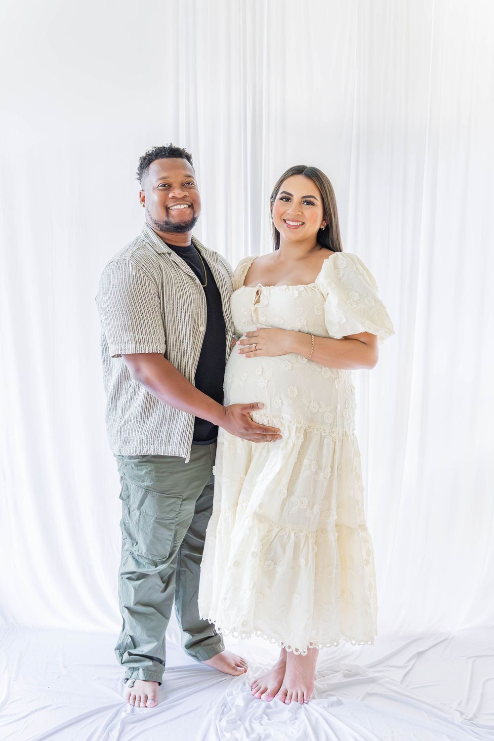 A couple shares tender moments in a bright white studio setting wearing coordinated casual outfits.