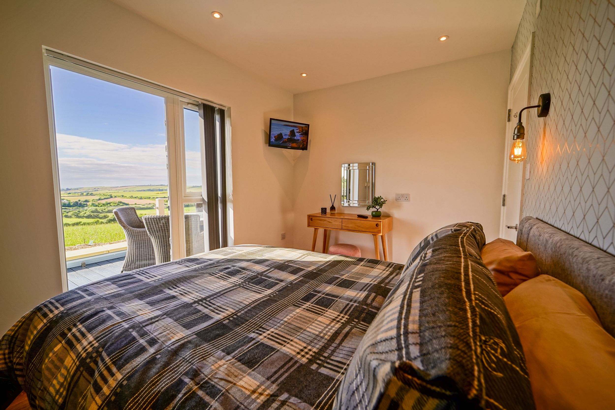 A modern bedroom with plaid bedding and large windows offering scenic countryside views.