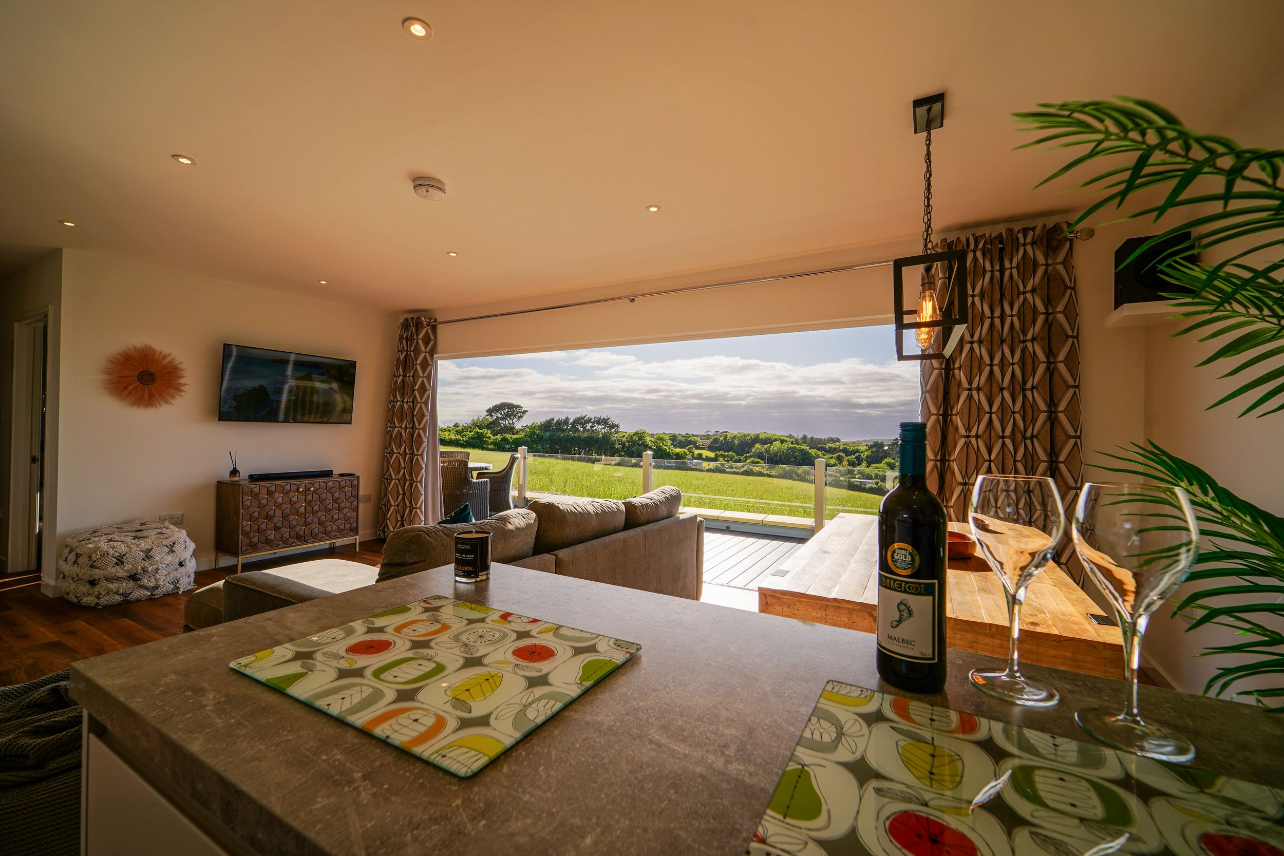 Luxurious living room with panoramic windows overlooking green landscape and colorful patterned rug.