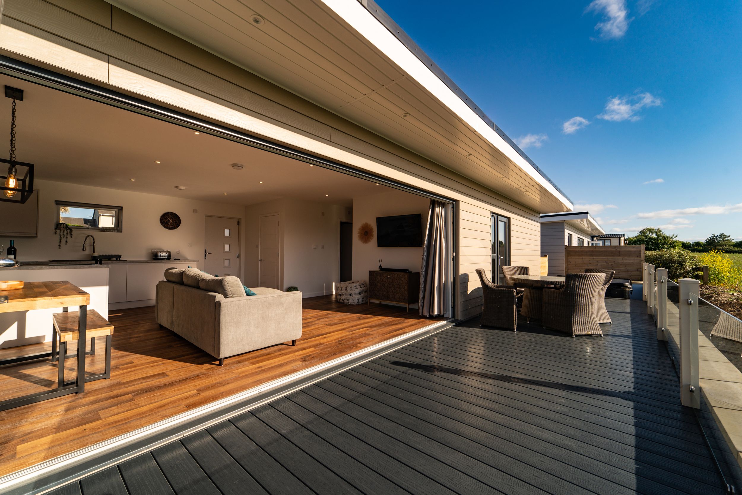 Modern deck with wooden flooring and sliding glass doors connecting to an open-plan living space.