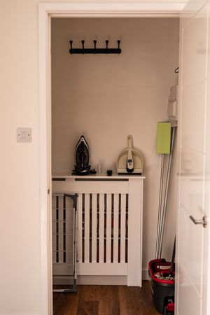 Utility closet with radiator cover, coat hooks, and household cleaning supplies.