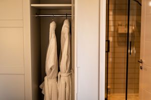 White bathrobes hanging in a modern built-in closet next to a glass shower door.