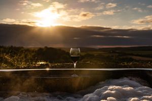 Wine glass silhouetted against a dramatic sunset sky over mountain landscape.